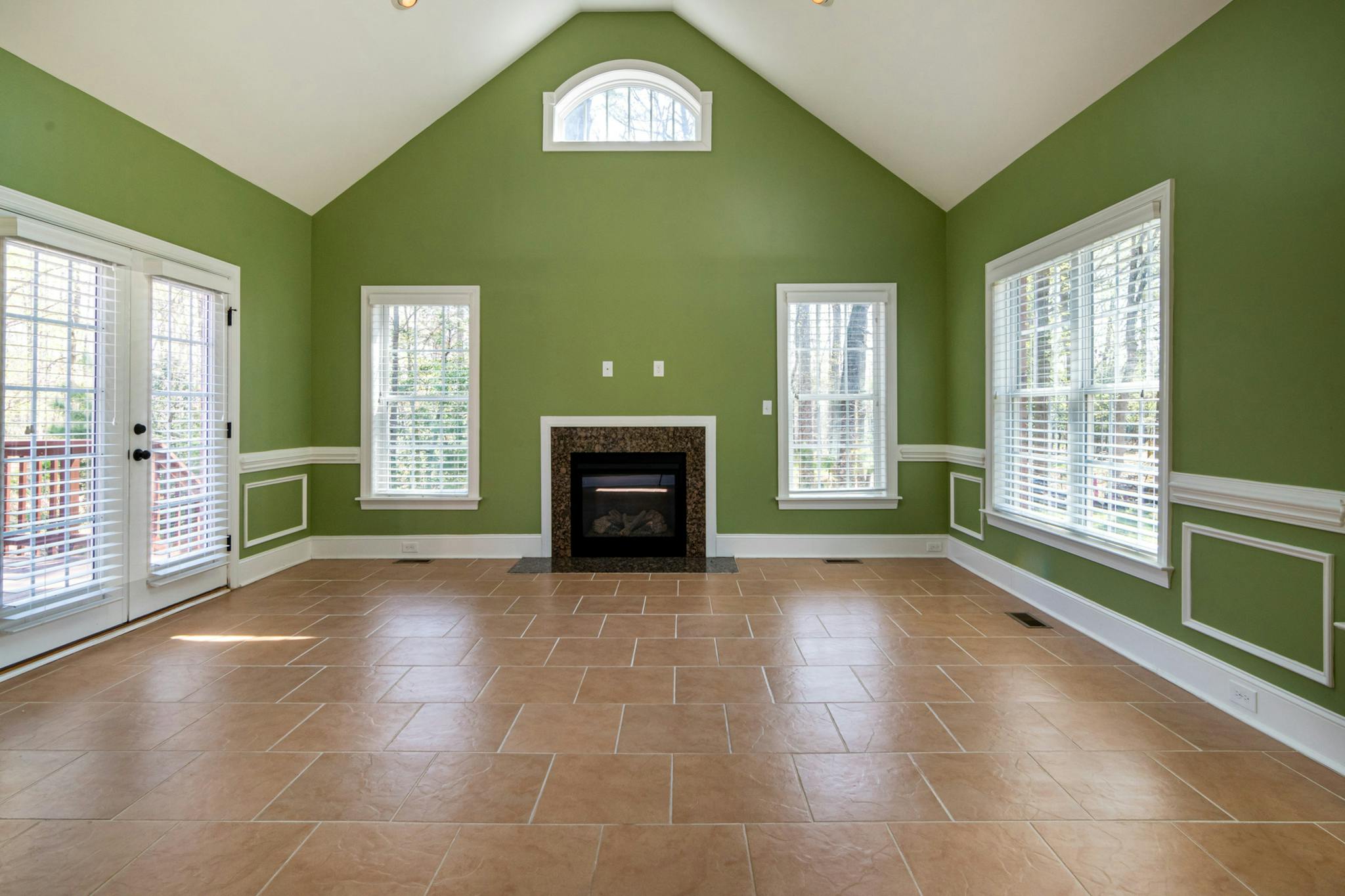Elegant empty living room featuring green walls, a fireplace, and tiled flooring.