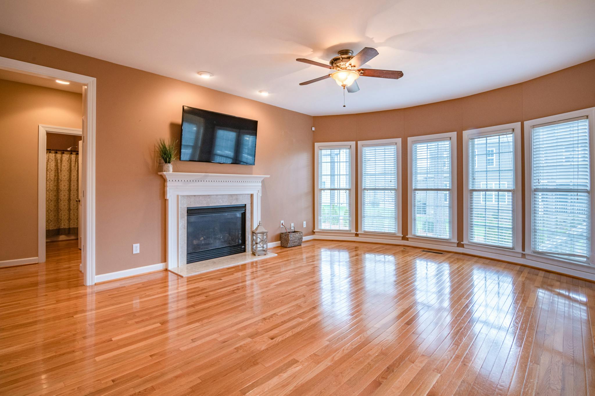 Bright living room with hardwood floors, fireplace, TV, and ceiling fan.